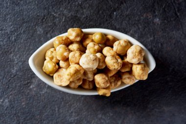 Koyu gri bir yüzey üzerinde beyaz bir seramik kasede kavrulmuş bezelyelerin yüksek açılı görüntüsü.