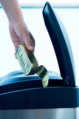 Genç beyaz bir adam boş bir teneke kutuyu paslanmaz çelik geri dönüşüm kutusuna atıyor.