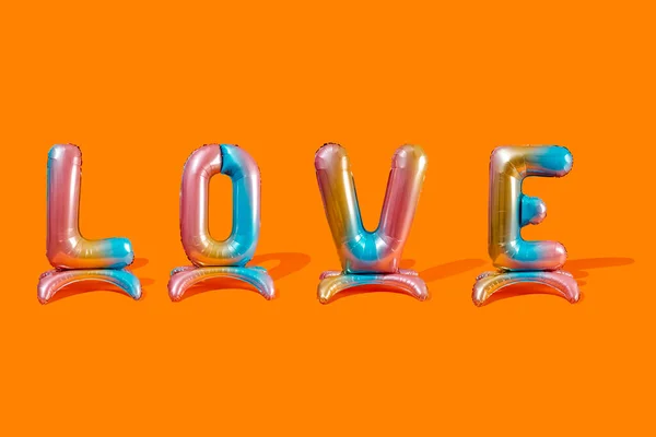 四个五颜六色的字母形气球 在橙色的背景上形成了爱这个词 — 图库照片