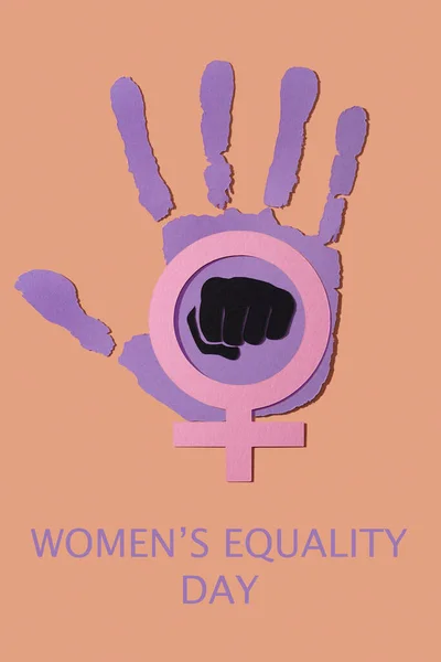 text womens equality day, a hand cut out in a violet paper, depicting the idea to stop the violence against women, a black fist depicting the idea of fight for equality and a pink female gender symbol