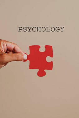 Metin psikolojisi ve elinde kırmızı yapboz parçasıyla soluk kahverengi arka planda beyaz bir adam.