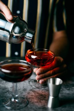 Kafkasyalı genç bir adamın yakın çekimi, çizgili bir gömlek giyiyor, bir kokteyl saklıyor, bir metal karıştırıcıdan, bir kokteyl bardağında