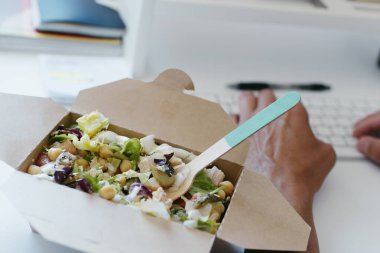 Kağıt bir kabın içindeki nohut salatasına yakın plan, masasında oturan genç beyaz bir adamın yanında.