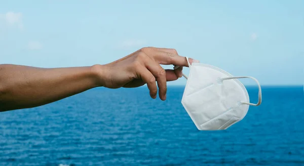 Joven Caucásico Sostiene Una Mascarilla Blanca Ffp2 Mano Frente Océano — Foto de Stock