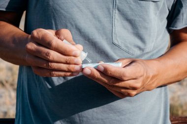 Kafkasyalı genç bir adamın açık havada dikilirken, gri bir tişört giyerken, kendi örneğini covid-19 antijen test cihazına yerleştirirken.