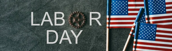 アメリカの小さな旗の横にある濃い灰色の背景にコグホイールが書かれたテキストの労働者の日は — ストック写真