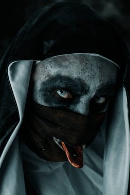 Tipik siyah beyaz giysili korkunç bir rahibeye yakın çekim. Siyah maskesindeki delikten dilini çıkartıyor.