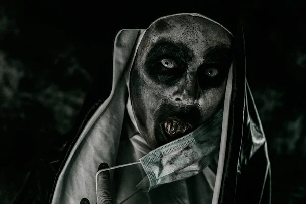 一个可怕的邪恶修女的特写镜头 她穿着黑白相间的衣服 用血淋淋的牙齿捂住她的嘴 戴着一个肮脏的一次性口罩 — 图库照片