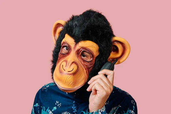 古い携帯電話で猿のマスクをした若者がピンクを背景に — ストック写真