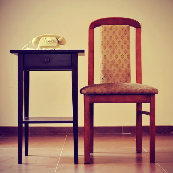 Old rotary dial telephone on a table next to a chair, with a ret — Stock Photo, Image