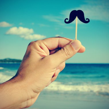 man hand with a fake moustache on the beach, with a filter effec clipart