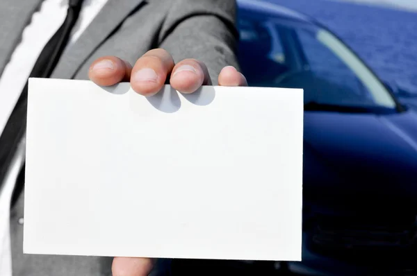 Hombre de traje sosteniendo un letrero en blanco con un coche en el backgrou — Foto de Stock