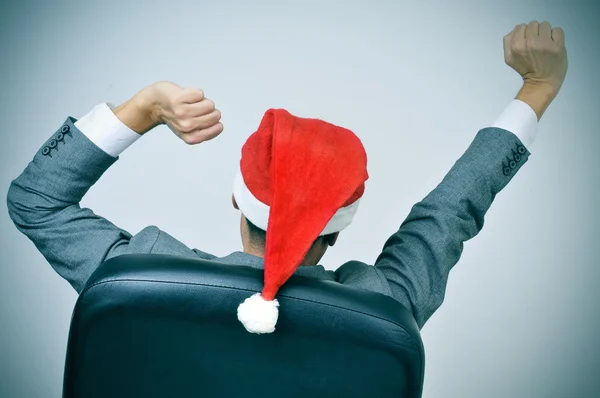Mężczyzna w kapeluszu santa rozciąganie ręce w jego krzesło biurowe — Zdjęcie stockowe