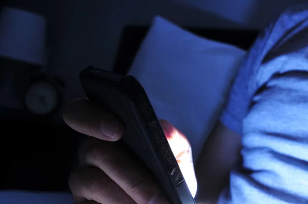Jovem usando seu smartphone na cama à noite — Fotografia de Stock