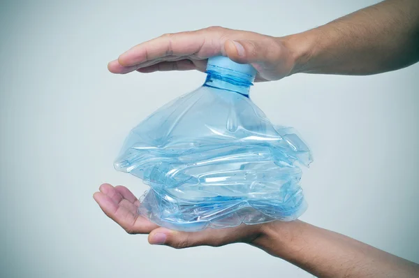 Joven rompiendo una botella de plástico con sus manos — Foto de Stock