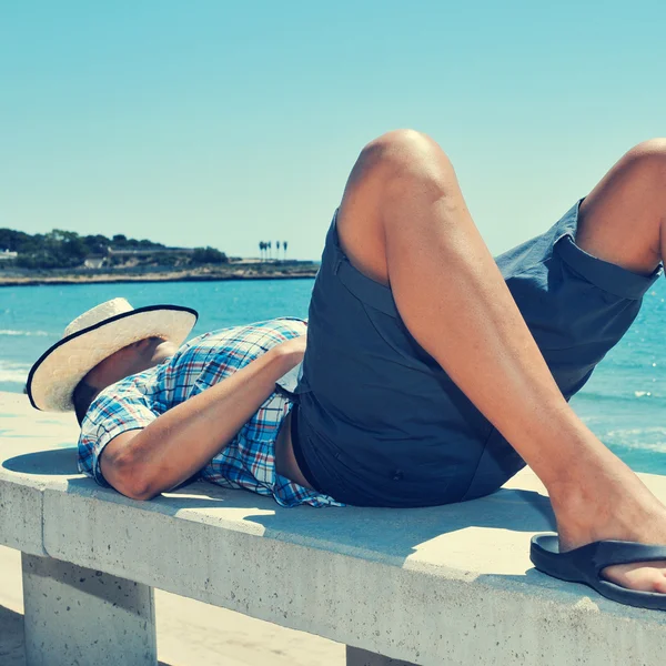 Junger Mann legt sich auf eine Bank in der Nähe des Meeres — Stockfoto