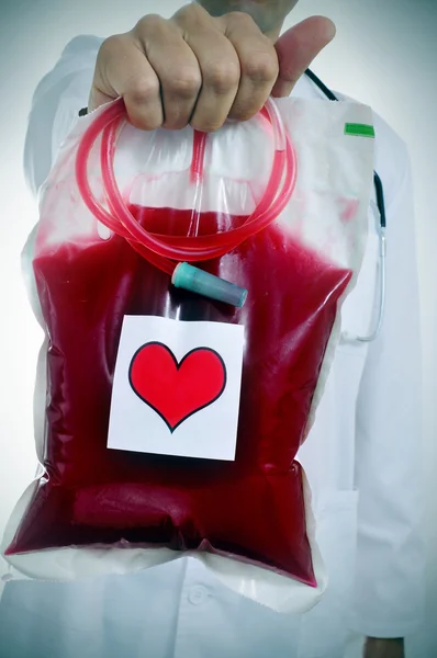 Doctor holding a blood bag with a sticker of a red heart — Stock Photo, Image