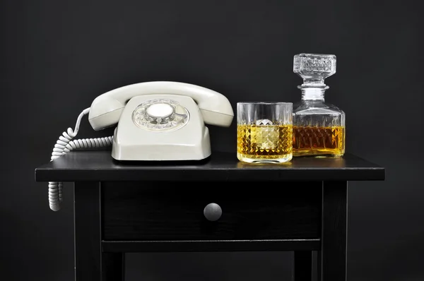 Een retro telefoon, een fles en een glas met drank op een tafel, — Stockfoto