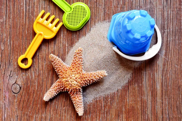 Starfish, sand and beach toys on a rustic wooden surface — Stok fotoğraf