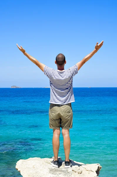 Man with his arms in the air in front of the ocean — Stockfoto