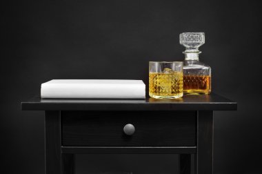 a book, a bottle and a glass with liquor on a table, over a blac