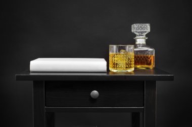a book, a bottle and a glass with liquor on a table, over a blac clipart
