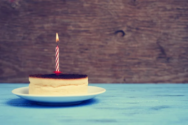 Candela di compleanno accesa su una torta di formaggio, con un effetto retrò — Foto Stock