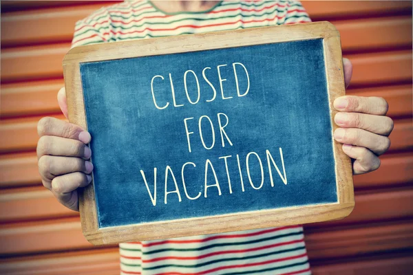 Young man with a chalkboard with the text closed for vacation — Stock Photo, Image