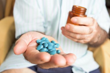 old man with a pile of blue pills in his hand clipart