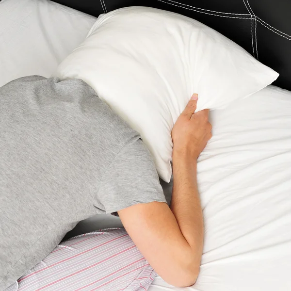 Young man face down in bed covering his head with a pillow — Stock Photo, Image