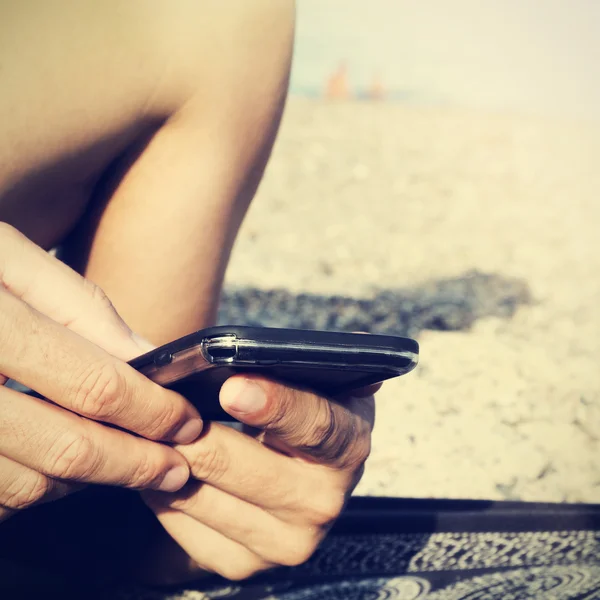 Sahilde bir akıllı telefon kullanan genç adam