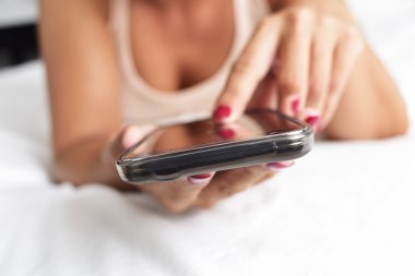 Genç bir kadın yatakta akıllı telefon kullanıyor.