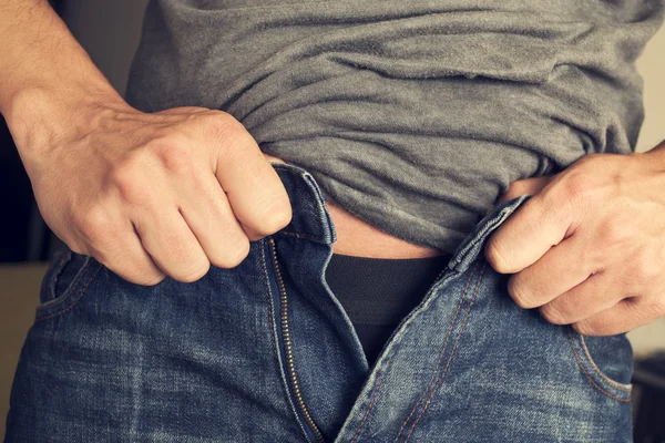 Young man trying to fasten his trousers — Stock Photo, Image