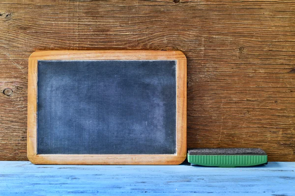 Blank chalkboard and an eraser on a blue wooden table — Stock Photo, Image
