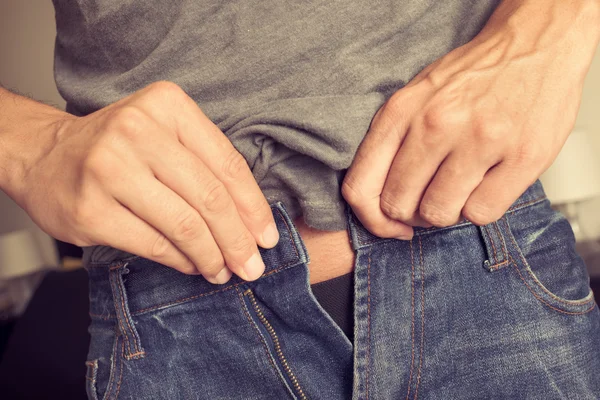 Young man trying to fasten his trousers — Stock Photo, Image