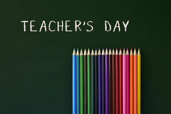 Lápis coloridos e professores de texto dia escrito em um chalkb verde — Fotografia de Stock