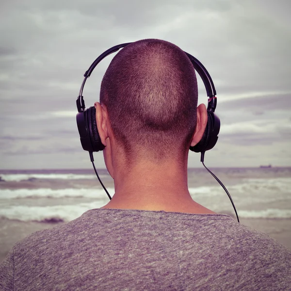 Ung man lyssnar på musik framför havet, filtreras — Stockfoto