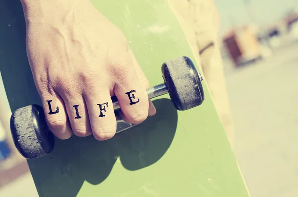 Young man with the word life tattooed in his hand with a skatebo — Stock Photo, Image