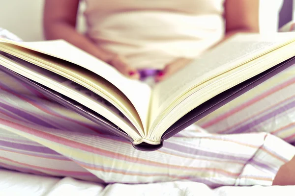 Νεαρή γυναίκα διαβάζει ένα βιβλίο στο κρεβάτι — Φωτογραφία Αρχείου