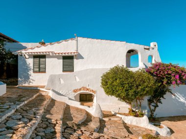 steps leading to white houses with green shutters and vibrant bougainvillea in La Almadrava, Hospitalet del Infant, Spain, on a sunny summer morning