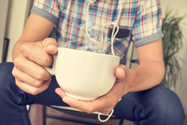 Ung man lyssnar på musik samtidigt ha en kaffe eller te — Stockfoto