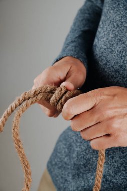 Kaygan düğümü jüt halatla bağlayan bir adam ellerini kapalı alandaki kaba doğal lif üzerinde dikkatlice çalışırken gösteriyor.