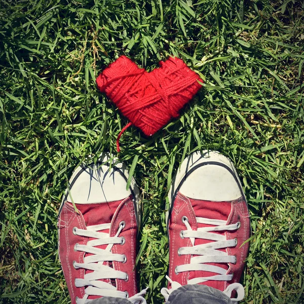 Man feet and heart-shaped coil of red cord on the grass, vignett — Stock Photo, Image
