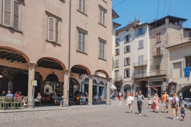 Bergamo, İtalya - 22 Haziran 2025: Citta Alta 'daki Piazza Mercato delle Scarpe manzarası, insanların geçitin altındaki gölgeli kafe masalarında yürüdüğü ve oturduğu, eski binalarla çevrili