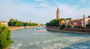 İtalya 'nın Verona kentinden akan Adige Nehri' nin geniş bir manzarası, sağda Citta Antica 'nın renkli evleri ve ağaçların tepesinden yükselen Basilica di Sant Anastasia' nın çan kulesi.