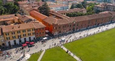 Pisa, İtalya - 26 Haziran 2025: Eğik Kule 'nin tepesinden görülen Piazza dei Miracoli, yürüme yolları, ortaçağ binaları ve merkez çimlerin etrafında hareket eden ziyaretçilerin bulunduğu kentsel bir manzara olarak gözler önüne seriliyor.
