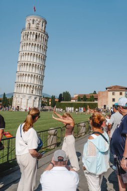 Pisa, İtalya - 26 Haziran 2025: Bir grup ziyaretçi, oyuncu perspektifli fotoğraflar için poz vererek, arkalarında daha fazla turist yürürken Eğik Pisa Kulesi 'ne doğru kollarını kaldırdılar
