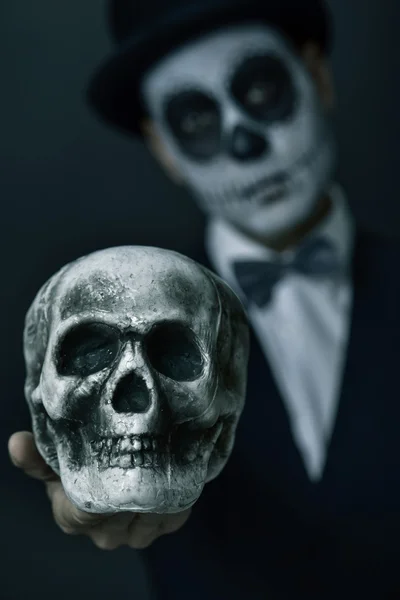 Hombre con calaveras mexicanas maquillaje mostrando un cráneo — Foto de Stock