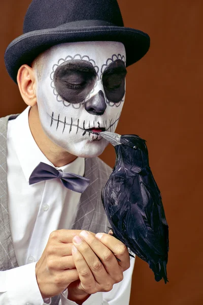 Hombre con calaveras mexicanas maquillaje besando a un cuervo negro —  Fotos de Stock