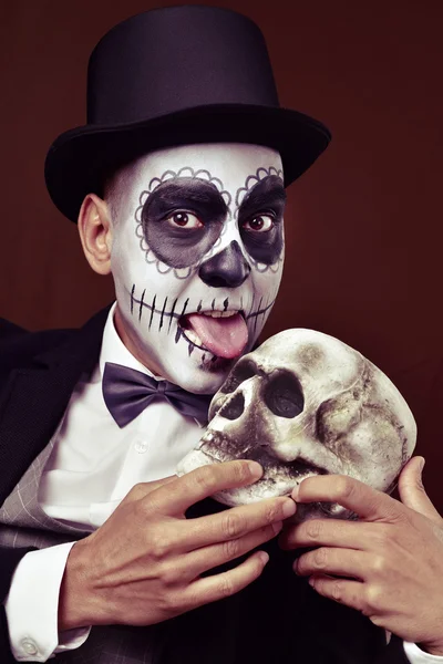 Hombre con calaveras mexicanas maquillaje lame un cráneo — Foto de Stock